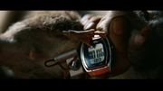 A close up of a rat with a cheap digital wristwatch strapped to it.